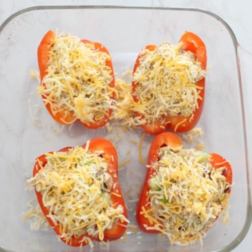 Tuna salad with cheese in 4 red bell peppers in a clear casserole dish