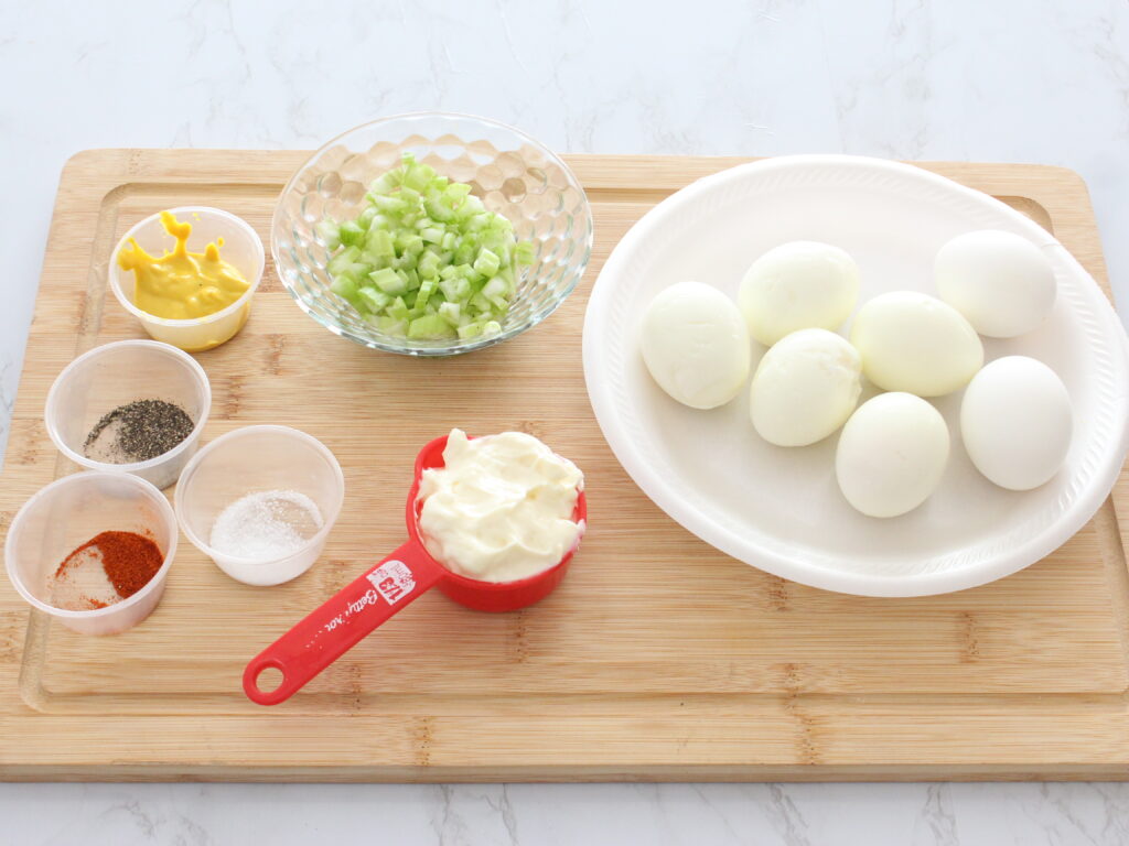 Hardboiled eggs surround by egg salad ingredients 