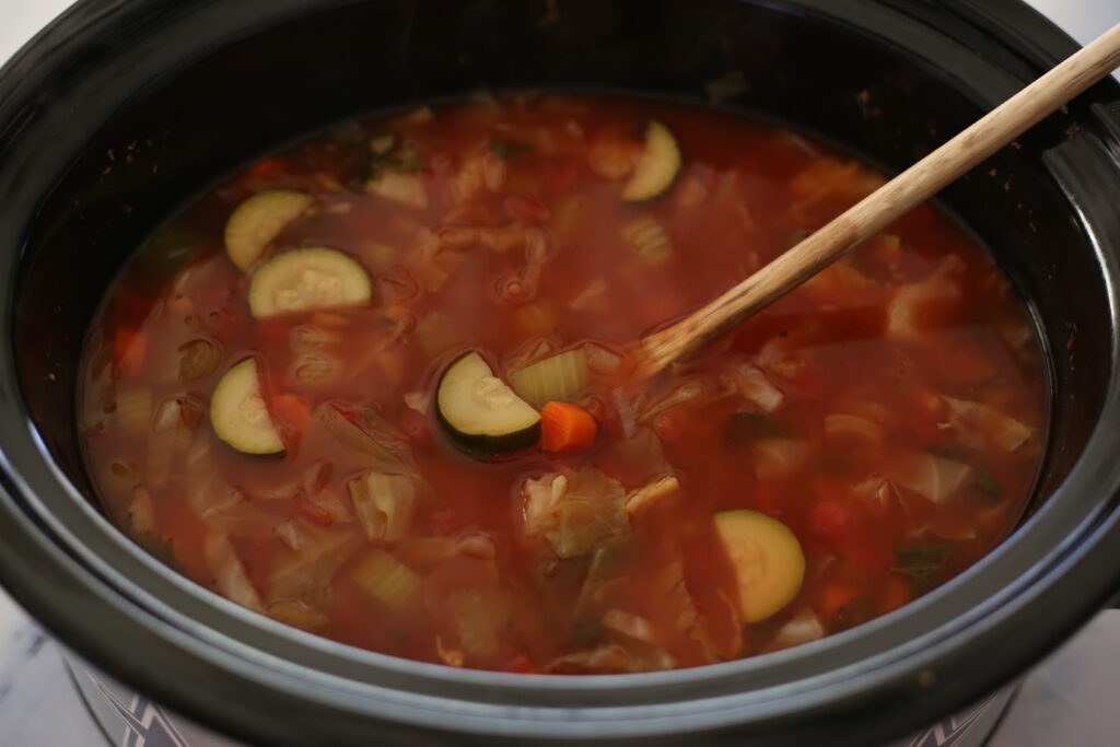 Zucchini and other vegetables in a red soup in a crockpot