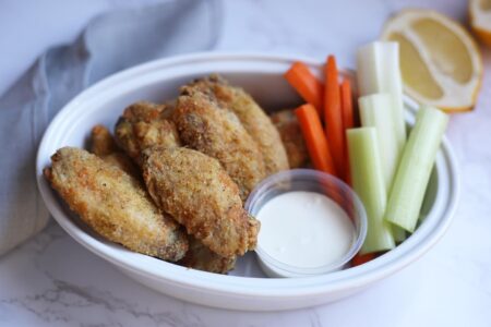 wings in a white oval bowl with ranch and vegetables