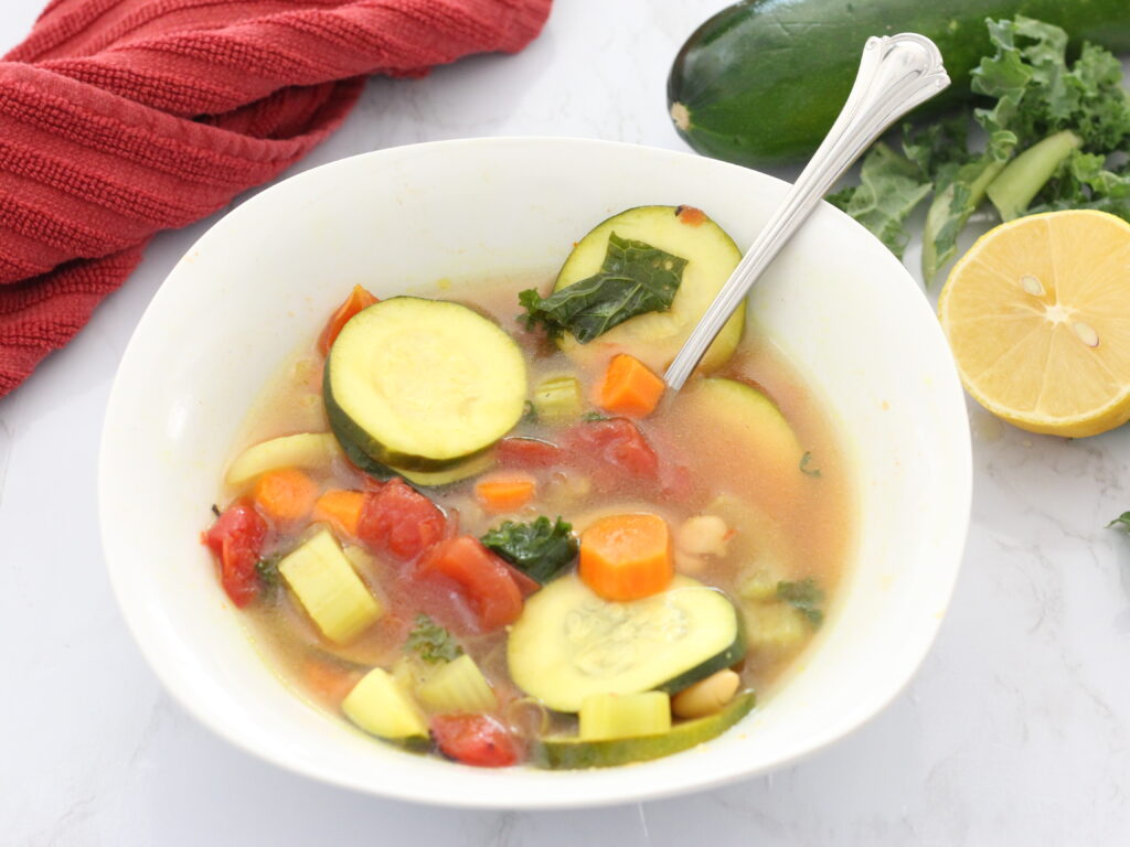 zucchini coins, carrots, and vegetables in broth in a white bowl with a spoon