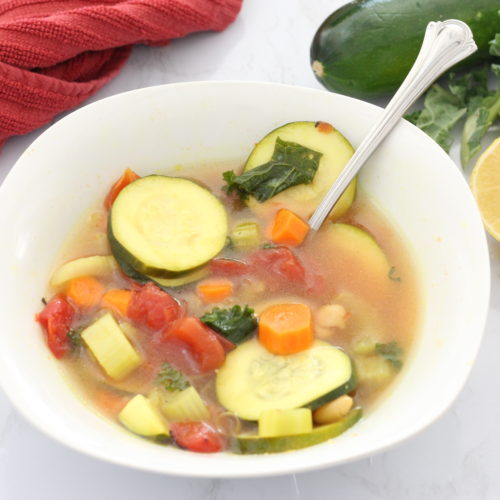 zucchini coins, carrots, and vegetables in broth in a white bowl with a spoon