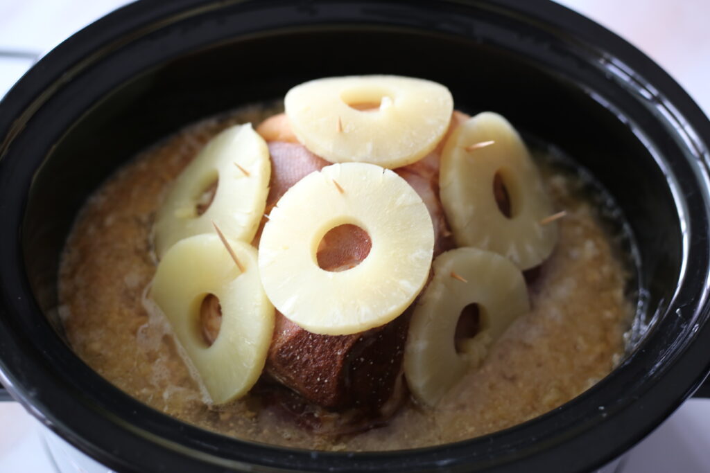 Ham inside a crockpot with pineapple slices on top.