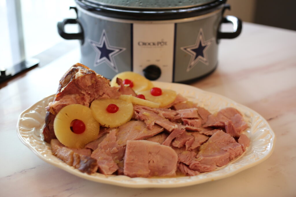 Ham sliced on a platter with a crockpot behind it on a table.