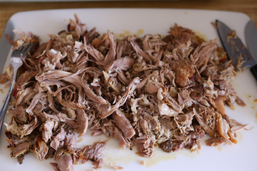 Shredded Puerto Rican Pork Roast on a plastic white cutting board. 