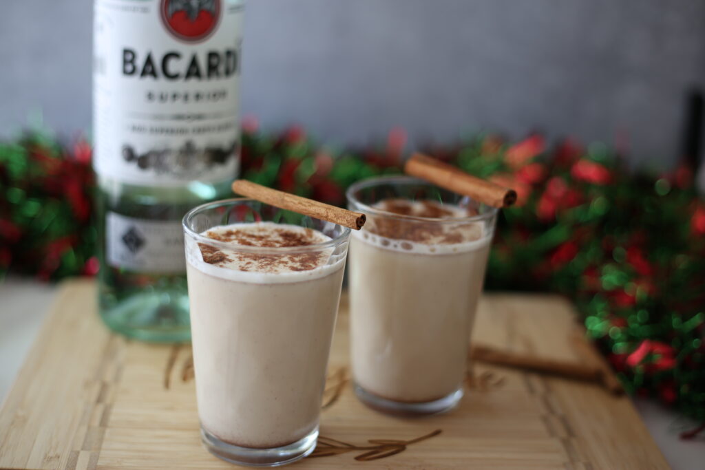 Coquito in a glass with a cinnamon stick as a garnish.