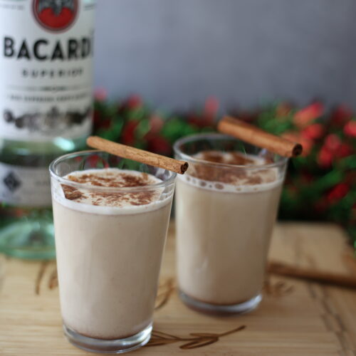 Coquito in a glass with a cinnamon stick as a garnish.