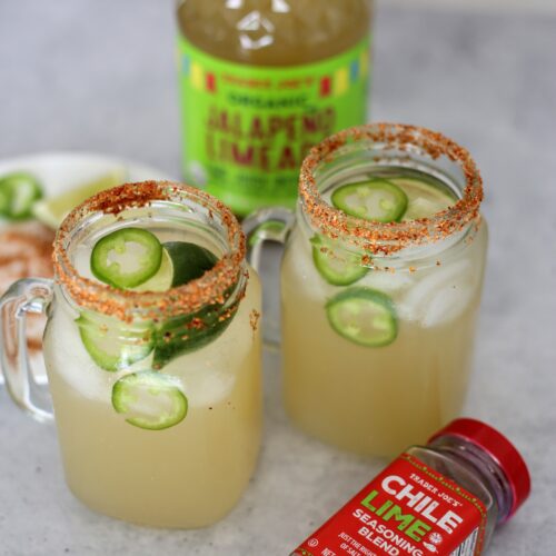 two mason jars filed with margarita drink with red salt around the rim.