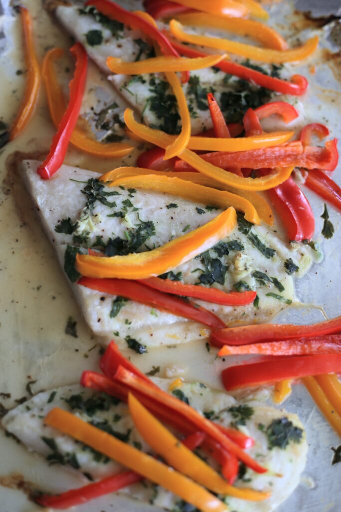 Fish with cilantro and red and orange sliced bell peppers on top.