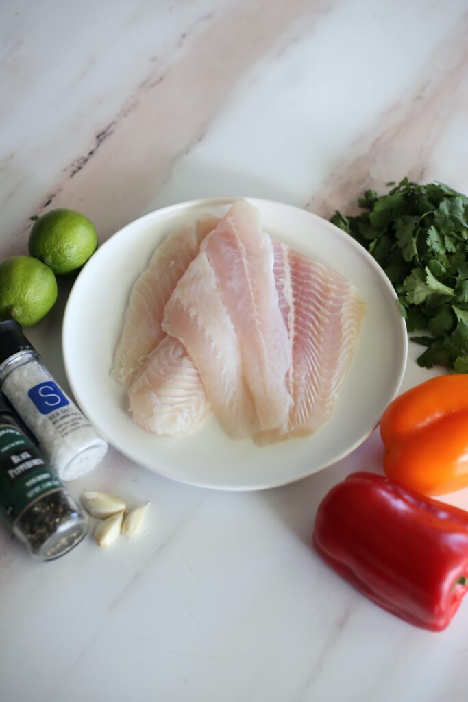 raw fish on a white plate surrounded by fresh ingredients.