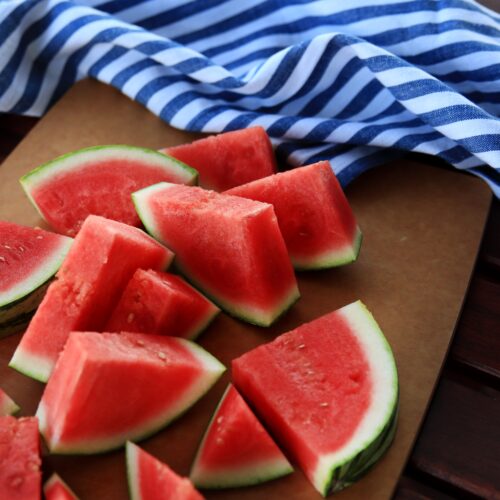 Watermelon cut in triangles on a brown cutting board with a blue dish towel on the side.