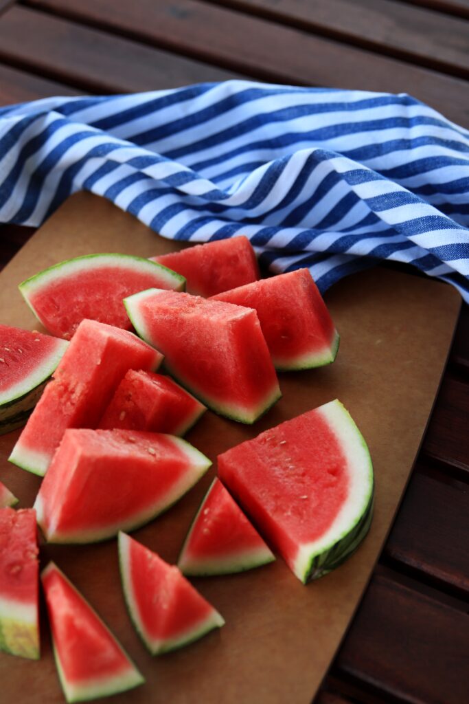 Watermelon cut in triangles on a brown cutting board with a blue dish towel on the side.