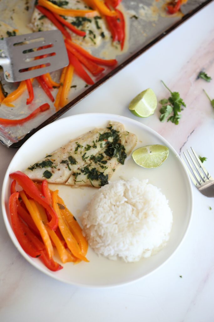 Cilantro lime baked fish on a white plate with colorful bell peppers and a side of white rice. 