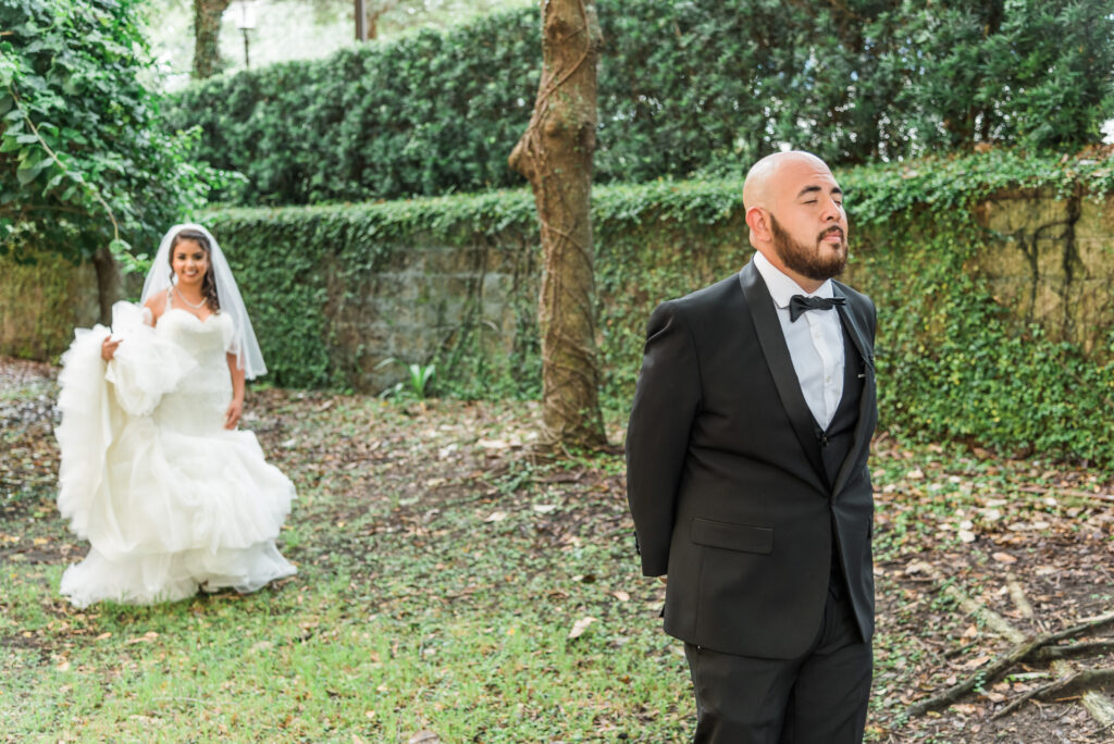 Bride walking up to groom with his eyes closed 