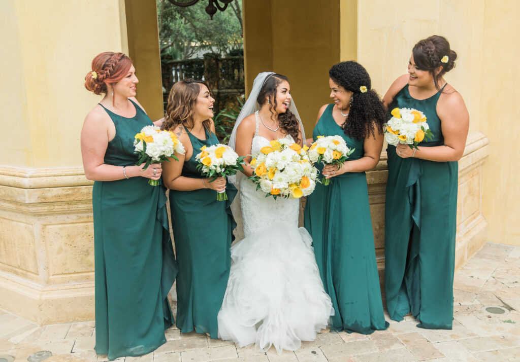 bride in a white dress with bridesmaids in green dresses outside posing together.