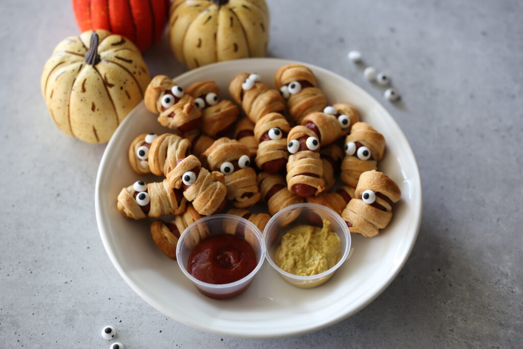 mummy dogs on a white plate with candy eyes.