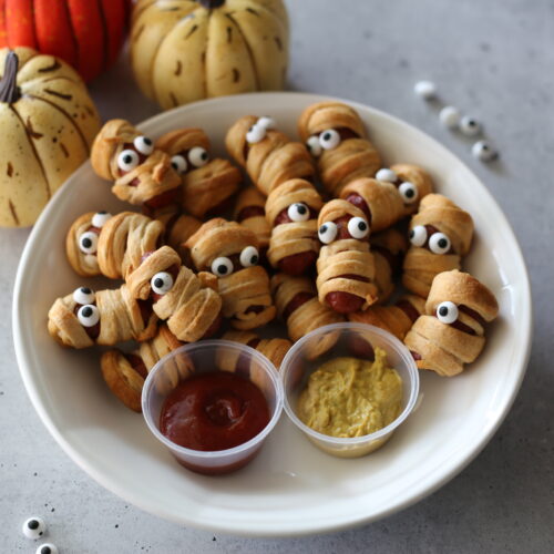 mummy dogs on a white plate with candy eyes.