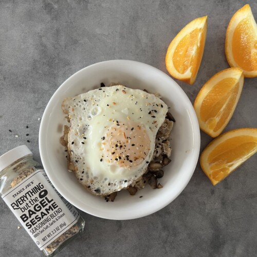 egg in a white bowl with everything but the bagel seasoning on top over oatmeal and a sliced orange next to it.